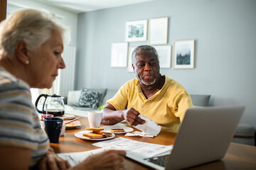 Diverse senior couple going over financials with laptop during breakfast