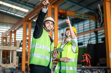 engineer, helmet, manufacturing, industrial, construction, colleagues, coworkers, discussion, hard hat, technician. Two workers in safety vests are pointing at something. They are wearing hard hats.