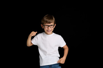 Fototapeta premium Smiling schoolboy in eyeglasses, wearing white t-shirt, isolated black background.
