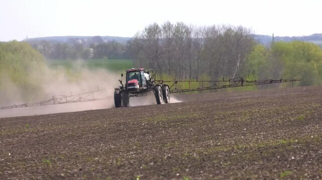 View of farming tractor spraying on field with sprayer, herbicides and pesticides at sunset. Farm machinery spraying insecticide to the green field, agricultural natural seasonal spring works-1
