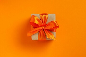 Top view photo of giftbox with orange satin ribbon bow on color background 