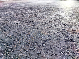 A close up view of an asphalt road surface, showing its rough texture and the sun reflecting off its surface. Background, texture, pattern, frame