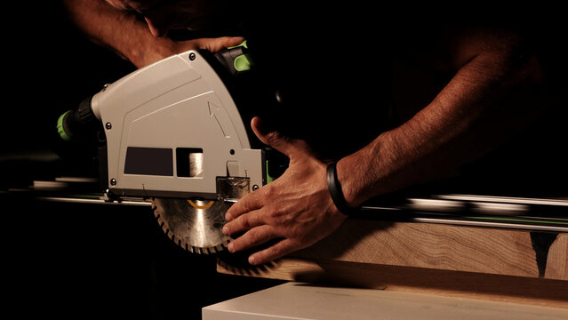 Construction Contractor Cutting To Size Wood Beam Using Portable Circular Saw Close Up. Worker using a circular saw to cut a wood in a factory with selective focus. Industrial Equipment Theme.