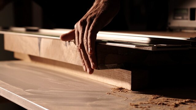Closeup hand gently glides over the wood, furniture production. man checks the quality of cutting and polishing a wooden surface. Professional carpenter cutting wooden board at sawmill. 
