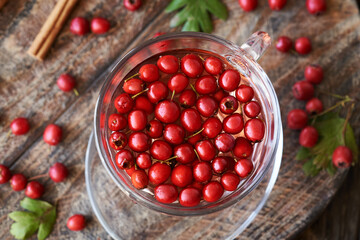 A cup of herbal tea with fresh hawthorn berries on a table in autumn