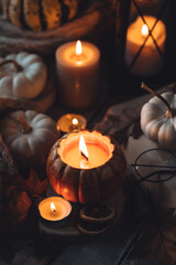 Cozy fall table decoration for Thanksgiving, romantic autumn home composition with small pumpkins, candles, wooden knitted sweater, book, dry leaves. Countryside rustic style