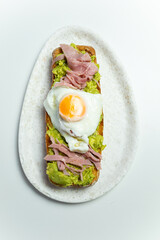 Overhead photograph of a toast of bread with fried egg, ham and avocado.