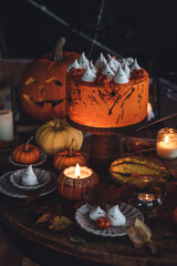 Homemade delicious chocolate cake with coloured orange cream and meringue ghosts, pumpkins for Halloween home party. Elegant beautiful table arrangement with candles, chandelier, Jack-o-Lantern