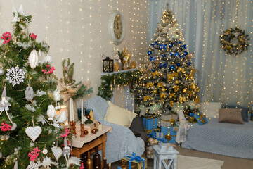 Two Christmas trees decorated in red white and blue golden colors, wooden toys, bows and bulbs. Wrapped presents below. Garland lights boke