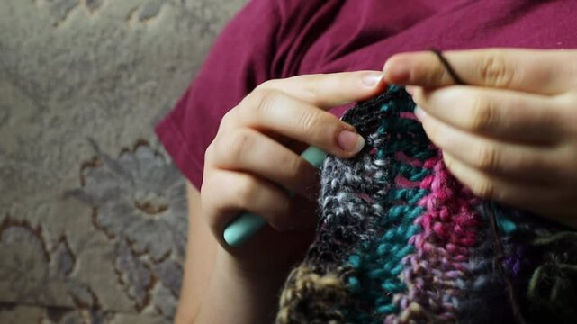 Young womans hands crochet colorful yarn with crocheting hook. Closeup details of handmade needlework art project and creative crafting techniques. Handmade textile artist nitting with yarn.