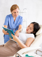 Obraz premium Friendly cosmetologist doctor offers girl patient to sign contract before the operation in a beauty clinic