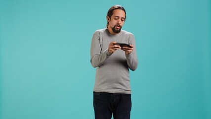Focused man plays intense videogame on mobile phone, spamming attack buttons on touchscreen. Gamer...
