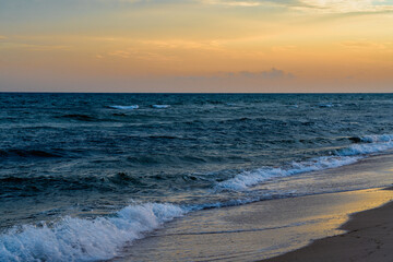 Golden sunset over gentle waves on a tranquil beach.