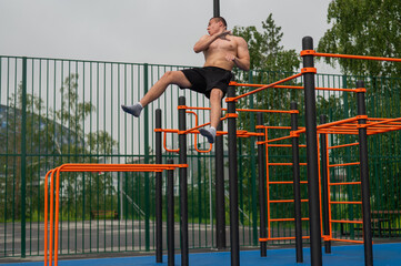 Fototapeta premium A shirtless man is doing a workout on the horizontal bars outdoors.