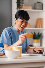 Asian female nurse online shopping on her laptop while working online from home