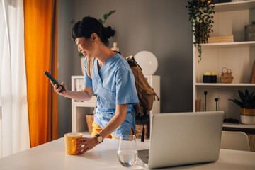 Asian woman medical professional checking phone and holding a mug in office.