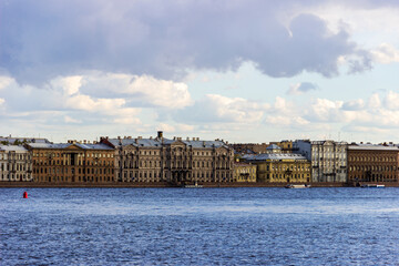 Fototapeta premium A panoramic view of the historic waterfront of St. Petersburg, Russia, showcasing rows of classic buildings along the Neva River under a partly cloudy sky.