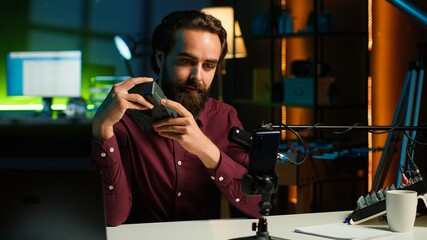 Tech guru presenting V mount battery, filming technology review using cellphone on tripod and professional microphone. Caucasian vlogger showcases charging device specs, recording with phone, camera A