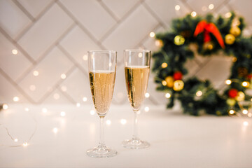 Two champagne glasses surrounded by sparkling lights with a Christmas wreath in the background