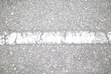 A close-up of a cracked white line painted on a gray asphalt road. The line is faded and worn, suggesting it has been there for a long time.