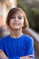 Smiling boy in blue shirt standing confidently with arms crossed outside school