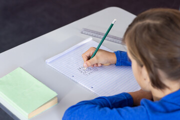 Writing math equations in notebook, boy focusing on schoolwork at desk