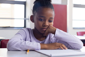 In school, african american girl sitting at desk looking at notebook, appearing thoughtful