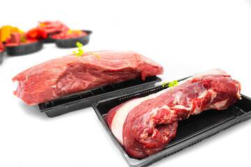 Side View of Fresh Beef Cuts in Black Trays with Background Ingredients on White Surface