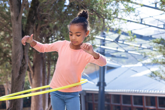 African american girl playing with hula hoop outdoors, enjoying physical activity at school - Powered by Adobe