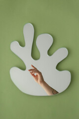 Hand Reaching Towards Abstract Mirror On Green Wall
