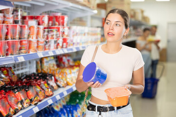 Interested young girl standing by shelves with colorful assortment of Asian noodles in store,...