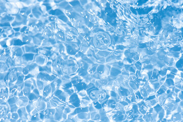 Blue water with ripples on the surface. Defocus blurred transparent blue colored clear calm water surface texture with splashes and bubbles. Water waves with shining pattern texture background.