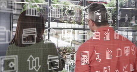 Image of business icons over diverse business people discussing work in office