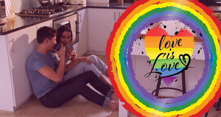 Image of love is love text and rainbow heart over diverse gay male couple talking in kitchen
