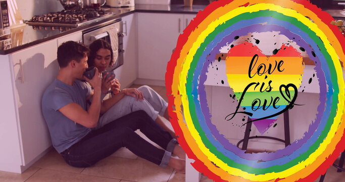 Image of love is love text and rainbow heart over diverse gay male couple talking in kitchen