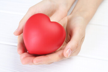 Woman holding red heart at white wooden table, closeup