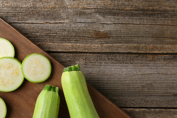 Board with fresh zucchinis on wooden table, top view. Space for text
