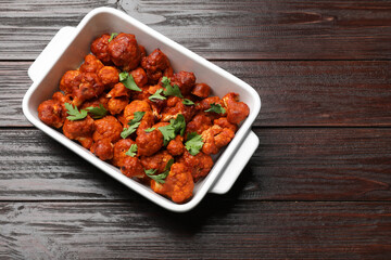 Baked cauliflower buffalo wings with parsley in baking dish on wooden table, top view. Space for text
