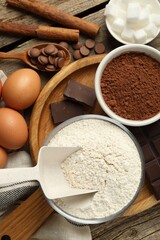 Flat lay composition with flour, cocoa and other ingredients for making dough on wooden table