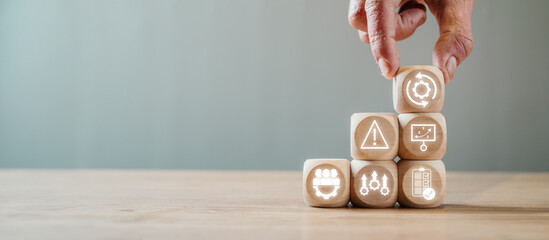 Hand stacking wooden blocks with icons representing business continuity, risk management, and strategic planning on a wooden table.