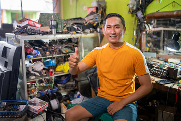 smiling Handsome Asian electronics repairman shows thumbs up at electronics service station