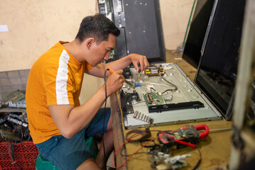 Asian man using soldering iron to repair led tv at service station