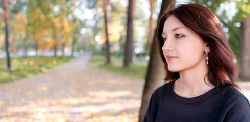 Portrait of a dark-haired girl in profile on the background of an autumn park with a parkway going off in the distance.