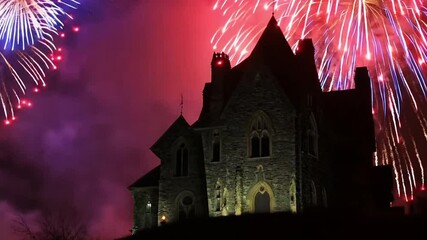 Vibrant fireworks bursting behind a silhouetted haunted house on a hill.
