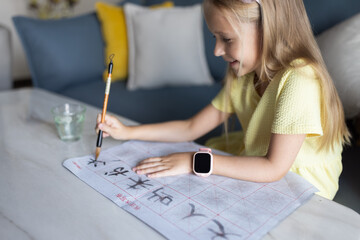 Cute little caucasian girl seven years old with blonde hair writing Chinese characters at home
