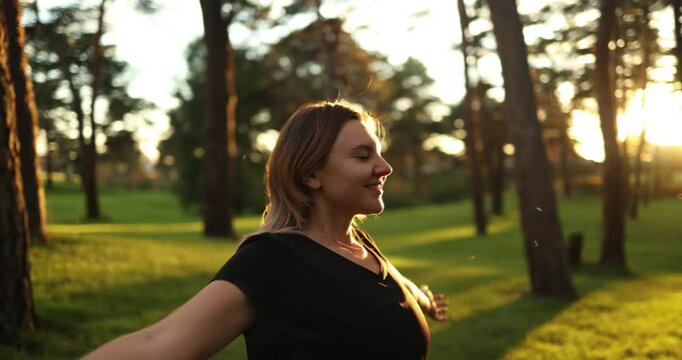 A woman experiences blissful and peaceful moments in a sunlit park, pleasantly surrounded by vibrant trees