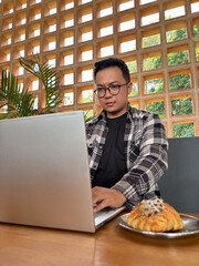 Man with serious expression looking at a laptop screen sitting in a cafe.