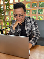 Man with a calm expression looking at a laptop screen sitting in a cafe.