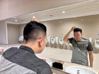 A man fixing hair with a large mirror in a public toilet
