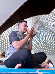 A Muslim man praying in a mosque in a seated position while raising both hands
